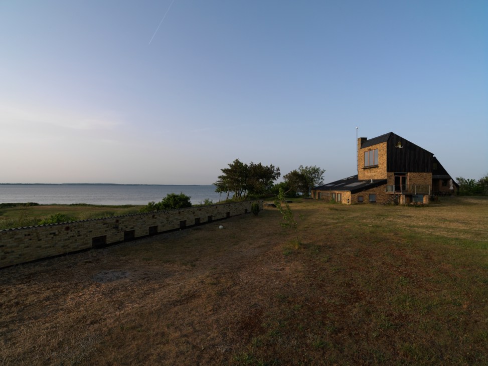 Brick house with black roof on grassy peninsula overlooking Limfjord in western Jutland.