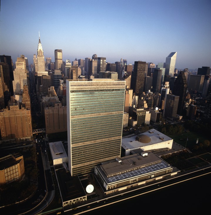 Aerial view of the UN headquarters building surrounded by Manhattan skyscrapers at dawn.
