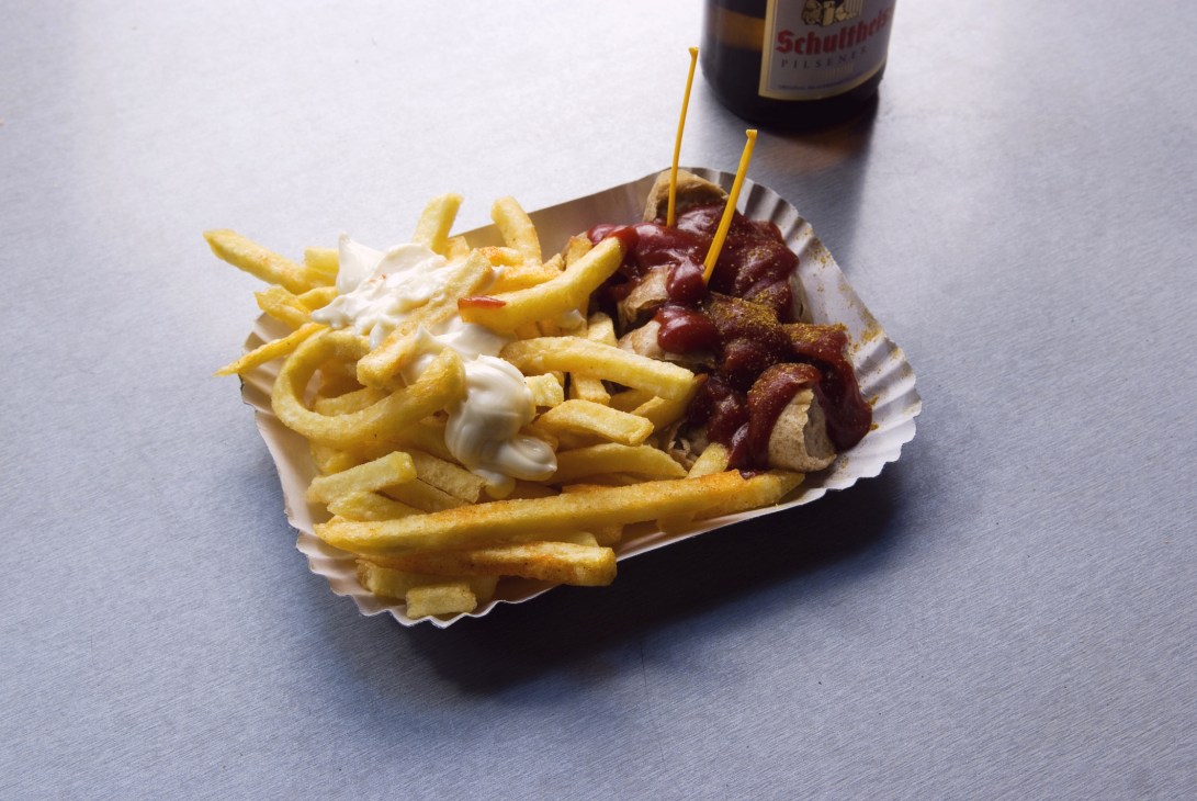 Currywurst with French fries and mayonnaise served in a paper container with a beer bottle.
