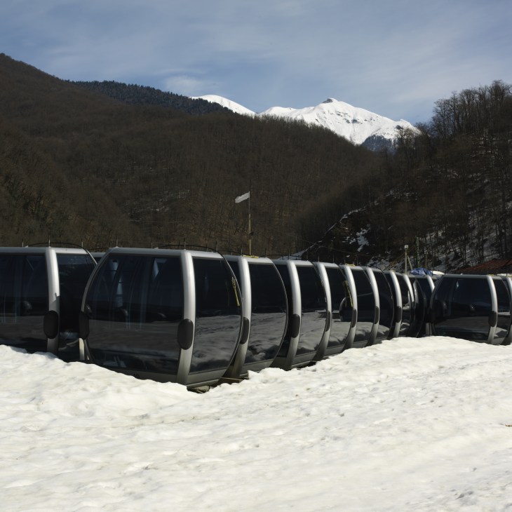 Multiple cable car cabins lined up in snow with snow-covered Caucasus peaks in background.