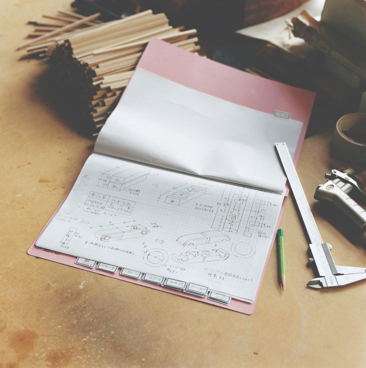 Detailed toy blueprints with hand-drawn sketches and measurements in a pink folder on a wooden workbench.