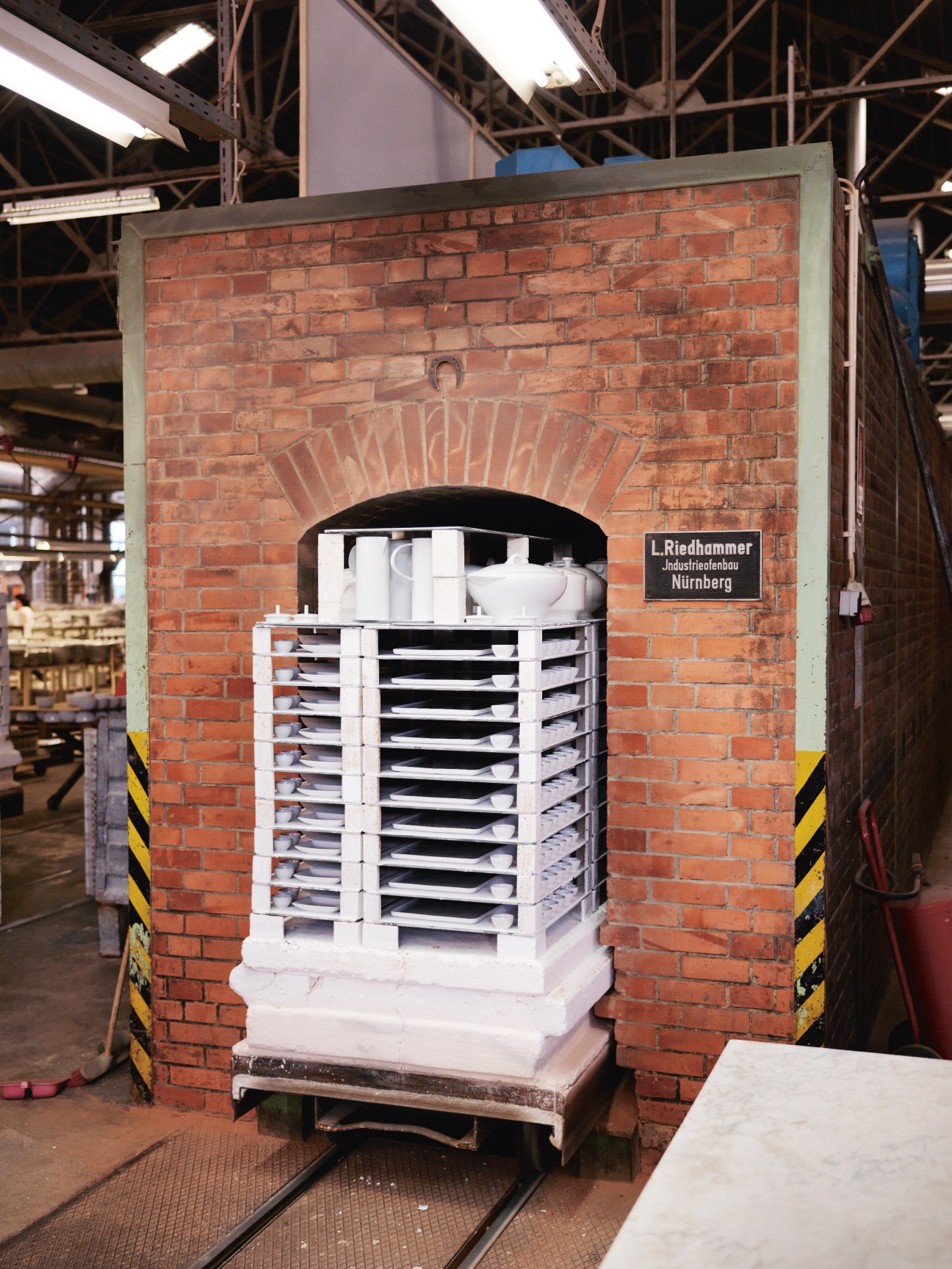 White porcelain coffee pots stacked on shelves inside a red brick kiln at Vista Alegre factory.