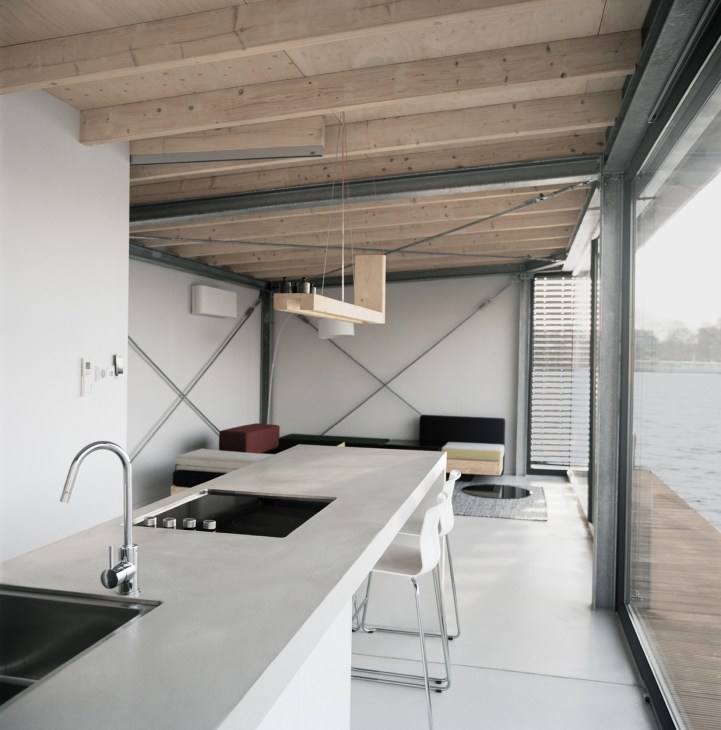 Interior of Flodd houseboat showing kitchen, dining area, wooden ceiling beams and floor-to-ceiling windows overlooking lake.