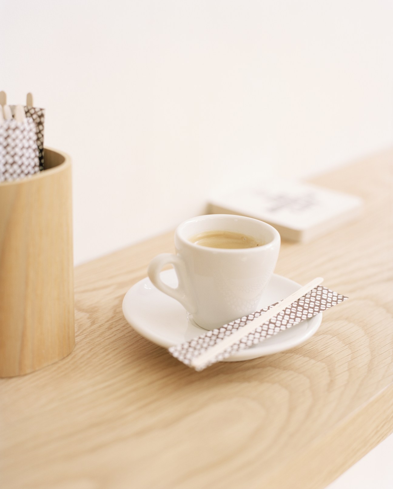 White Hasami porcelain cup and saucer with espresso on a wooden table next to a wooden utensil holder.