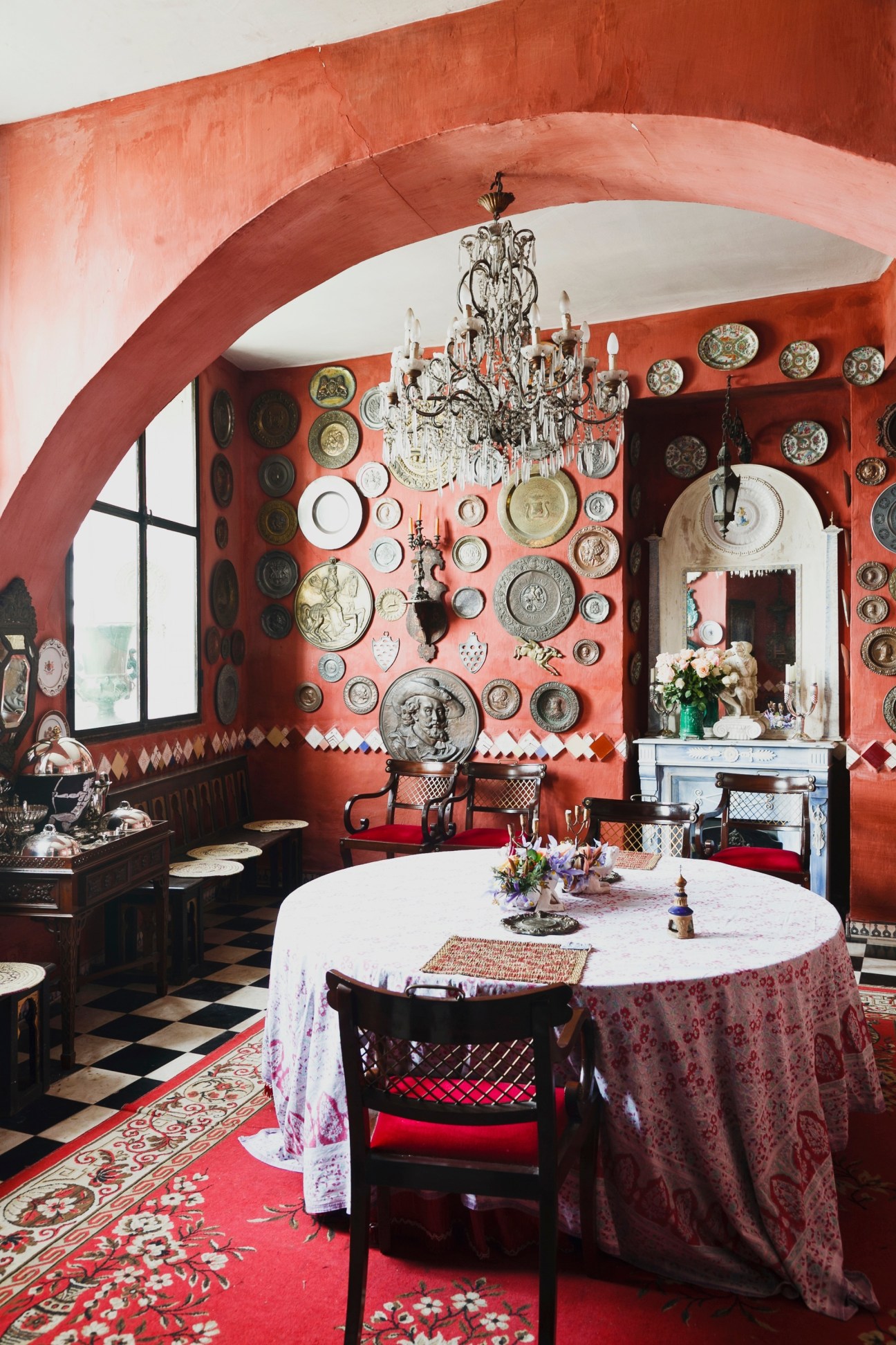 Living room with terracotta walls, ornate chandelier, and decorative plates displayed on walls