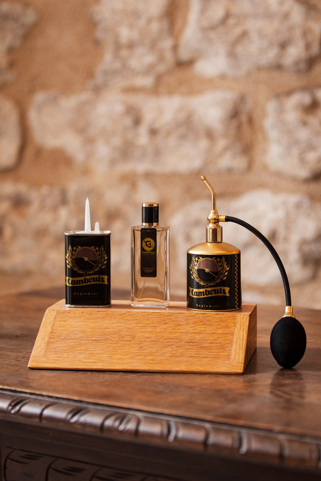 Cambouis perfume collection by Didier Gaglewski displayed on wooden stand with stone wall backdrop.