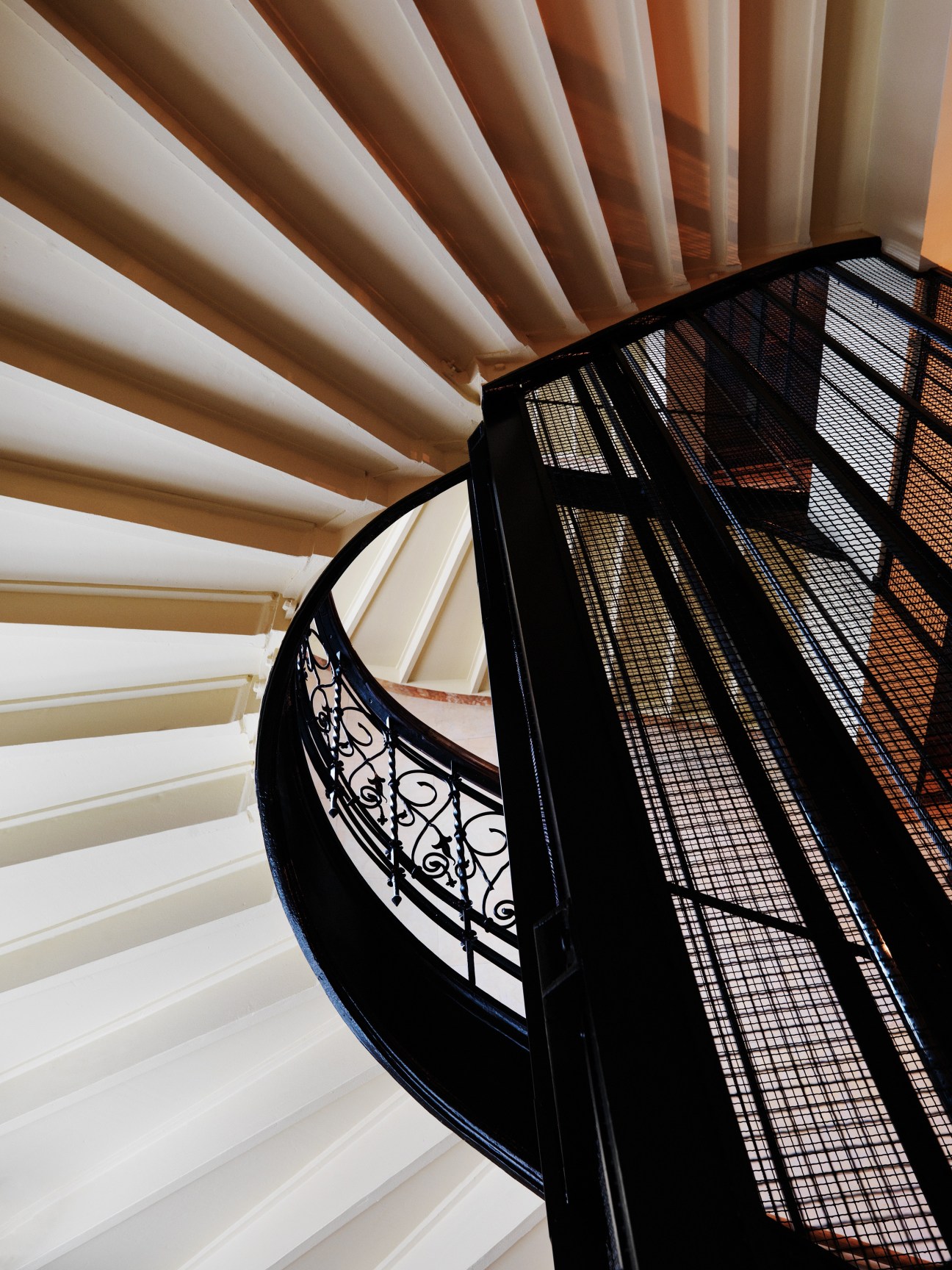 Spiral staircase with ornate wrought iron railings and mesh lift shaft in the Straw Hat Factory renovation.