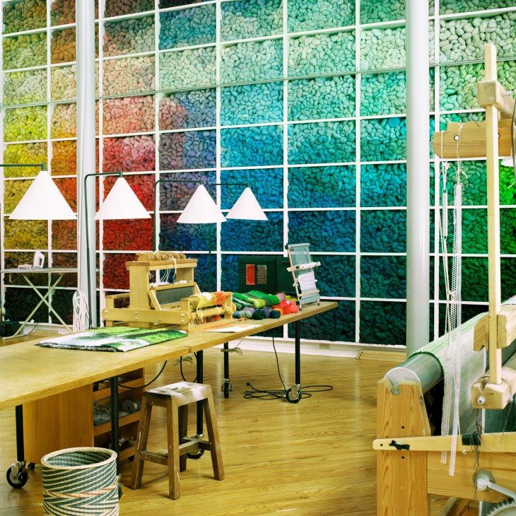 Helena Hernmarck's studio featuring a floor-to-ceiling grid wall display of colored wool yarn in vibrant hues.