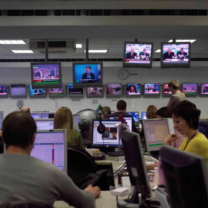Russia Today newsroom with staff at desks monitoring multiple screens displaying news broadcasts and feeds.