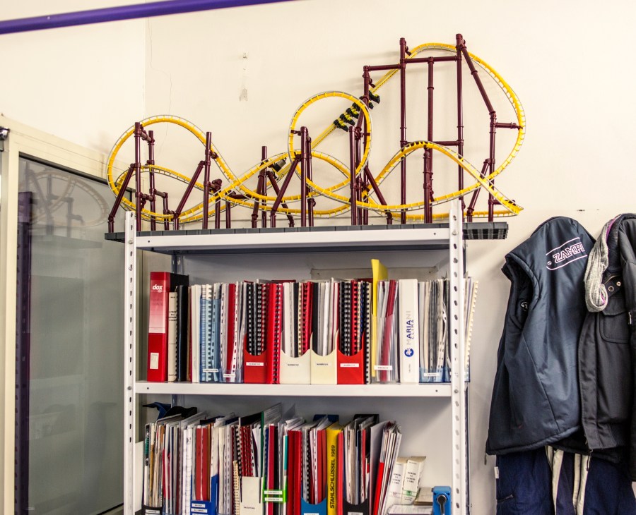 Roller coaster mock-up with yellow track and purple structural supports displayed above shelving in Zamperla design office