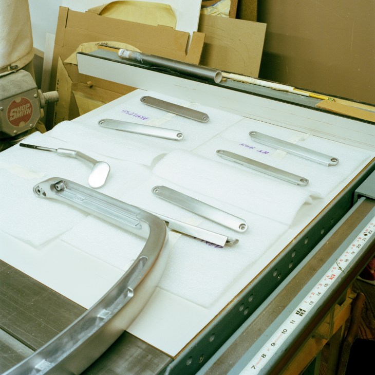 Various metal chair components and armrest parts laid out on white paper in a workshop.