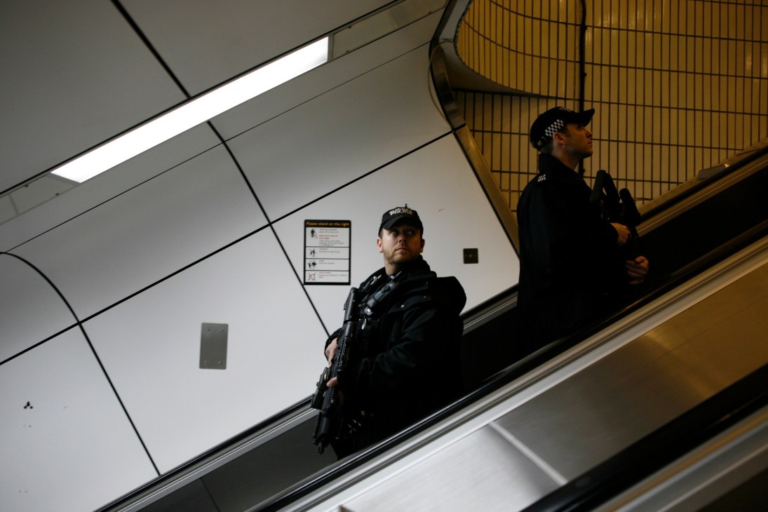 Armed police officers with assault rifles stand on an escalator at Gatwick station.