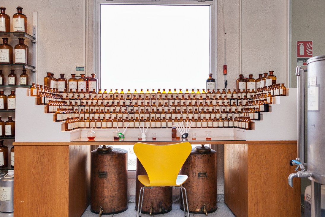 A perfume organ at Parfumerie Fragonard with hundreds of amber glass bottles arranged on wooden shelves behind a yellow chair.
