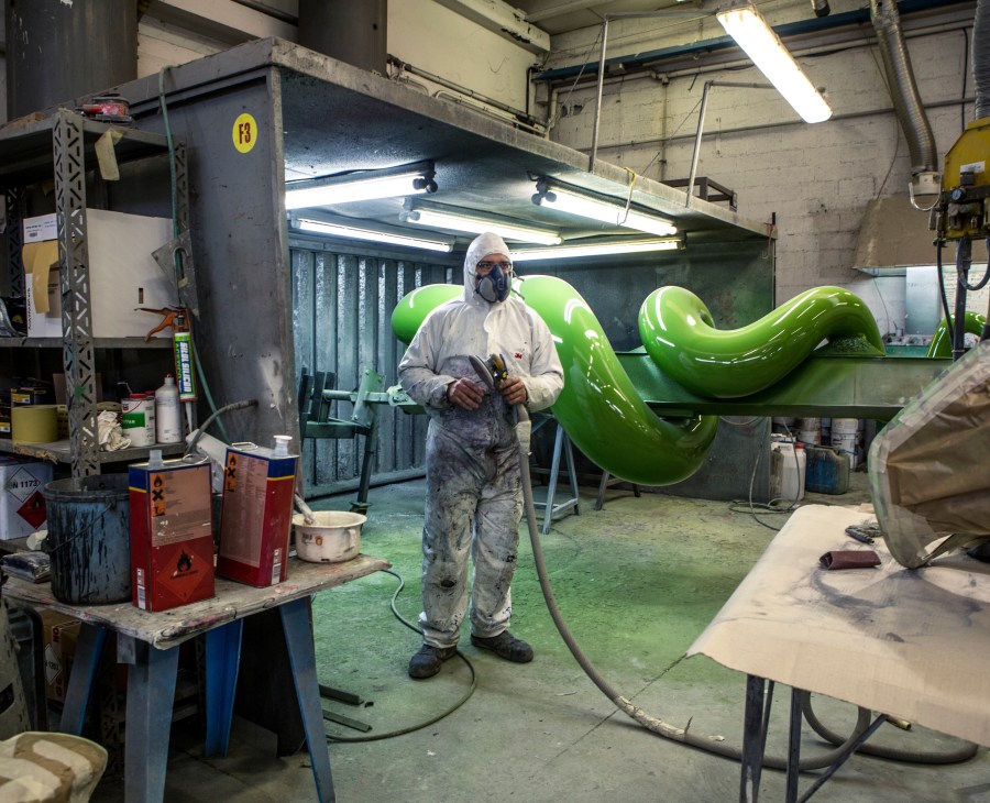 Worker in protective suit and mask spraying a bright green ride component in the Zamperla paint shop.