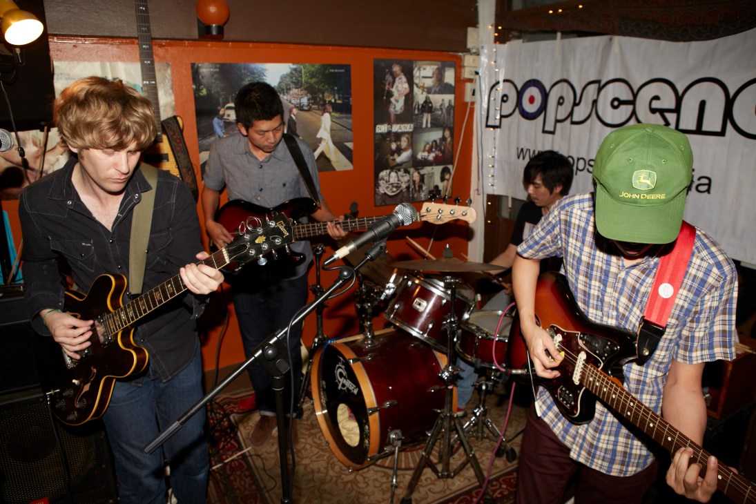 Basement Tape band performing live with guitarists and drummer on stage at an indoor venue.
