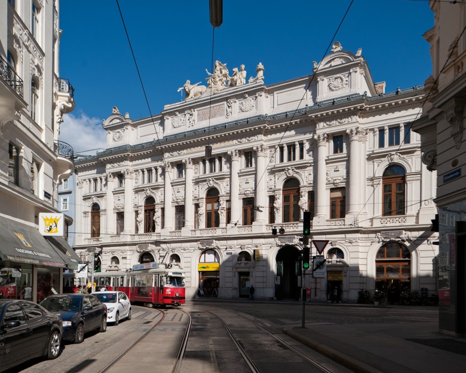 A Viennese street with ornate historic buildings, a red tram, and tramlines under a clear blue sky.