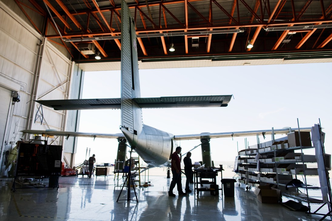 Twin Otter aircraft under construction in a factory hangar with workers assembling the fuselage and wings.