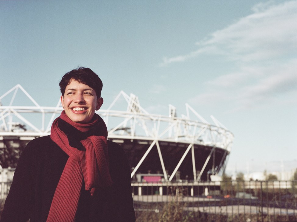 Eleanor Fawcett smiles at the camera wearing a red scarf, with the Olympic Stadium visible behind her.