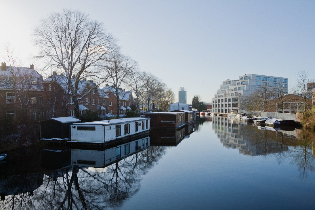 Houseboats moored on a still canal in Amsterdam Noord with modern apartment buildings reflected in the water.