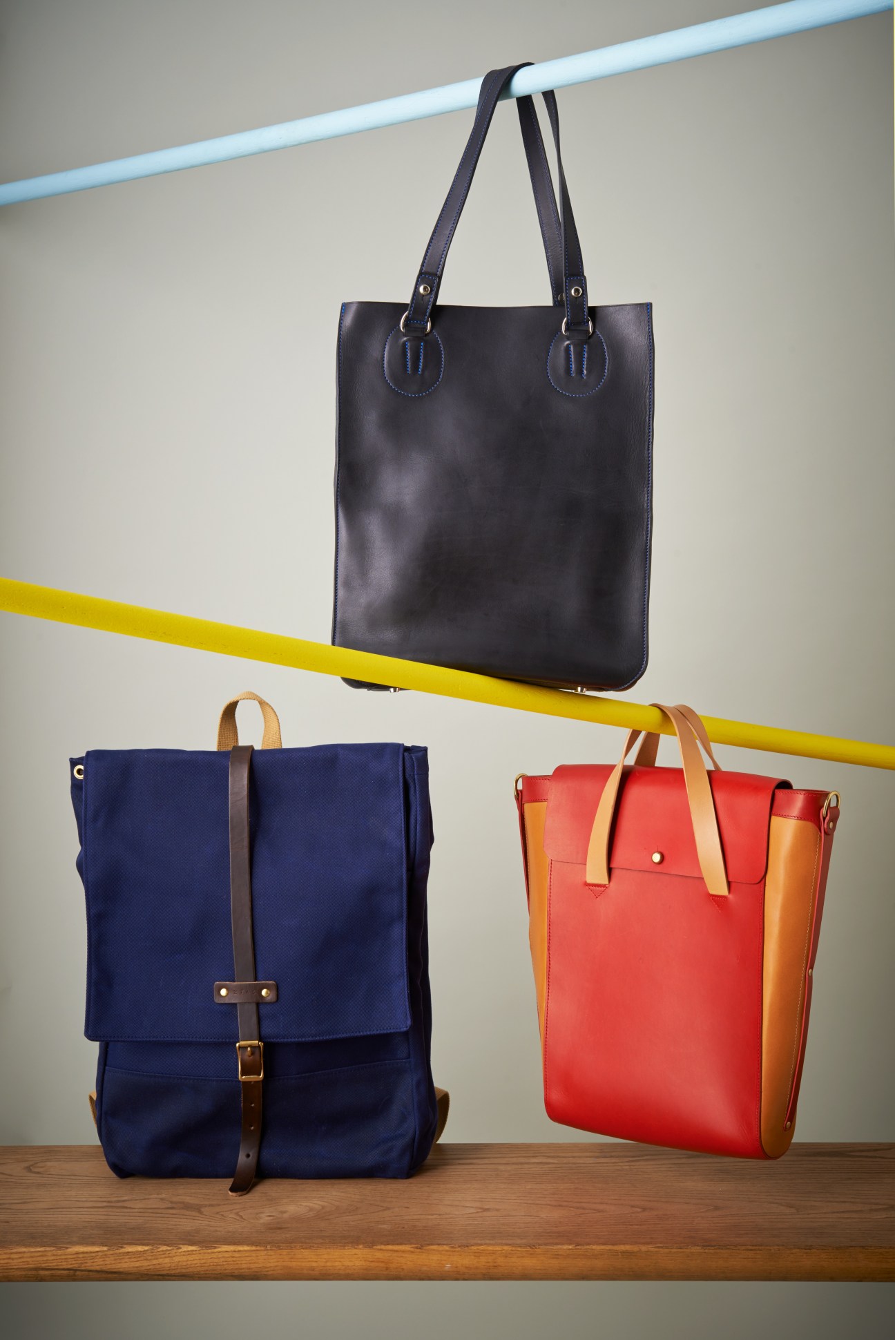 Three leather bags in different styles and colors displayed against a gray wall with colored lines.
