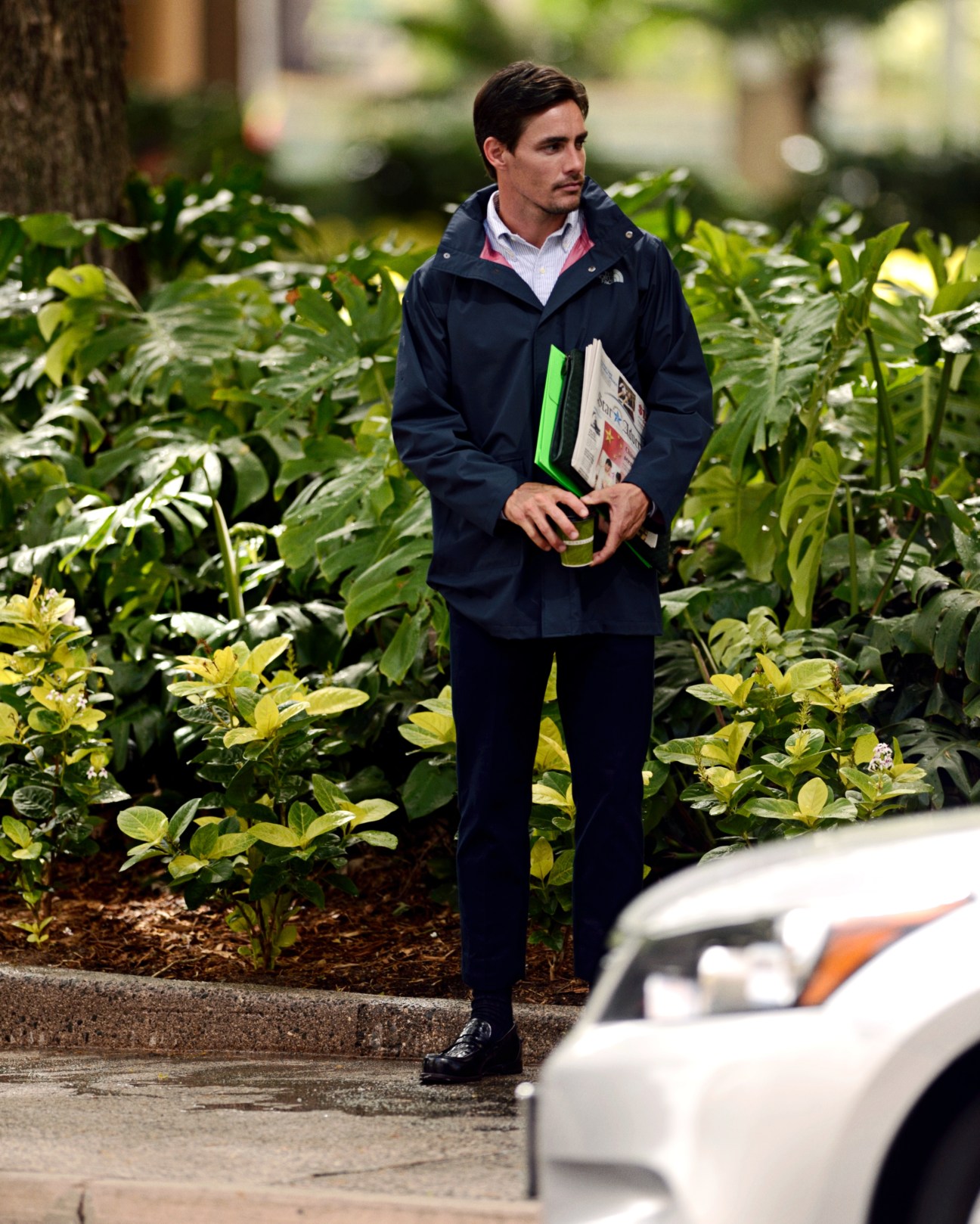 Man in navy Ermenegildo Zegna suit and Brooks Brothers shirt holding Bottega Veneta document case in garden setting.