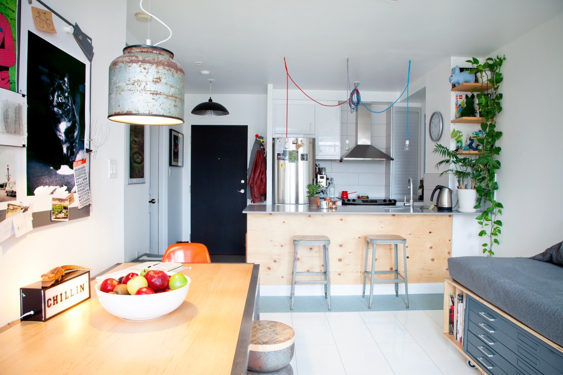 Modern kitchen and living area with light wood island, stainless steel appliances, and hanging colorful wire art installations.