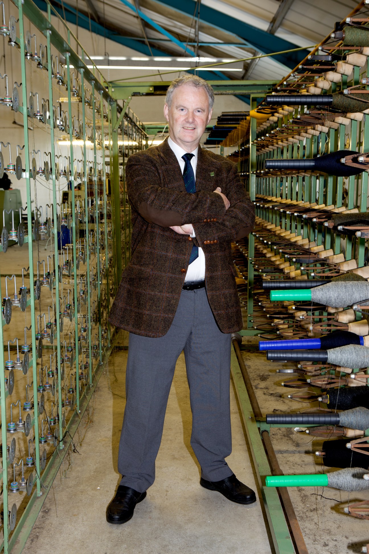 Rae Mackenzie, sales director of Harris Tweed Hebrides' mill at Shawbost, standing in front of yarn spools on industrial looms.