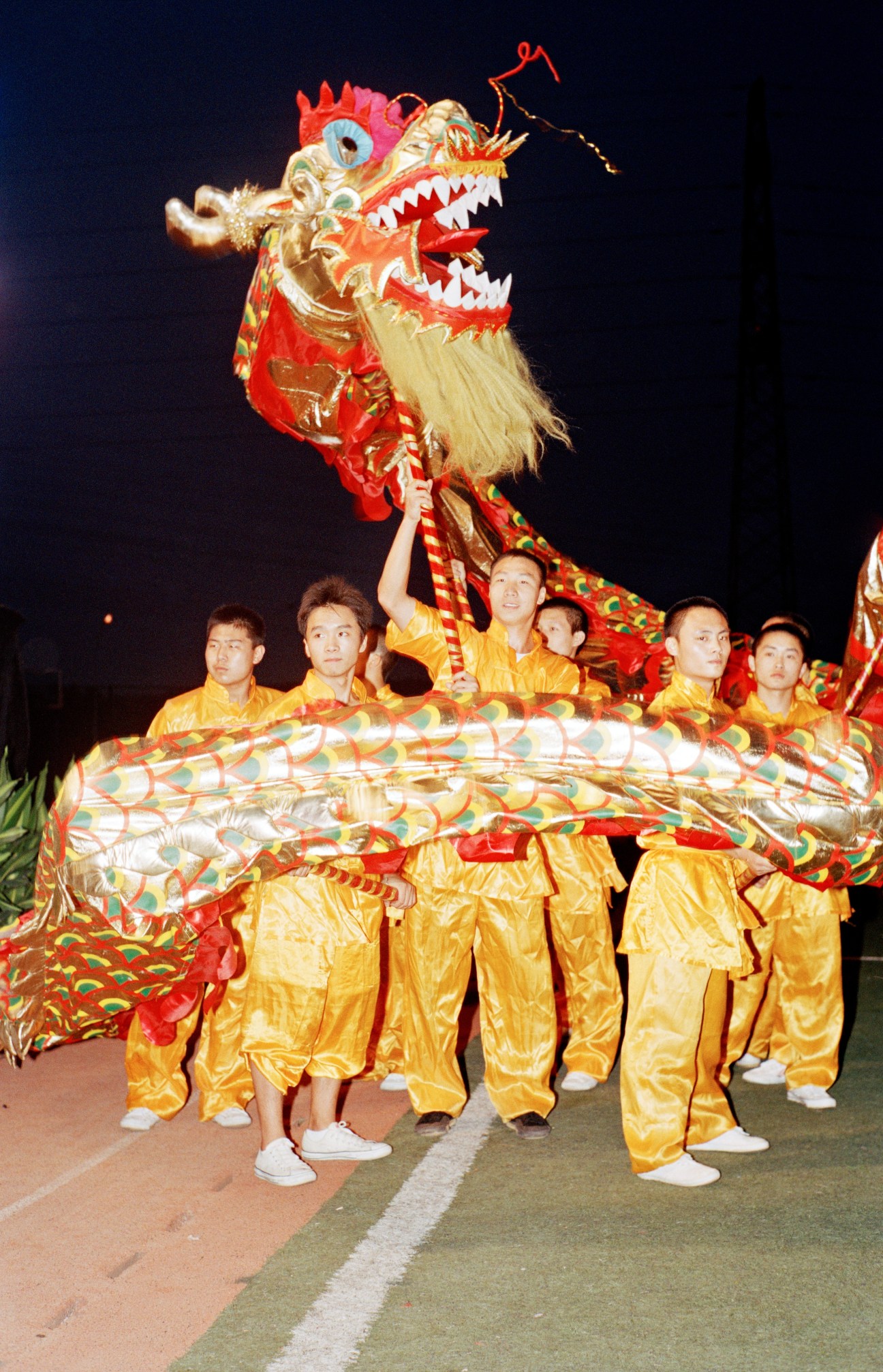 Performers in yellow costumes hold up a large red and gold dragon puppet during a nighttime ceremony.