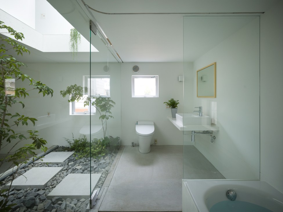 Modern bathroom with indoor garden courtyard featuring plants, coarse stones, concrete stepping stones, glass shower enclosure, and natural skylight.