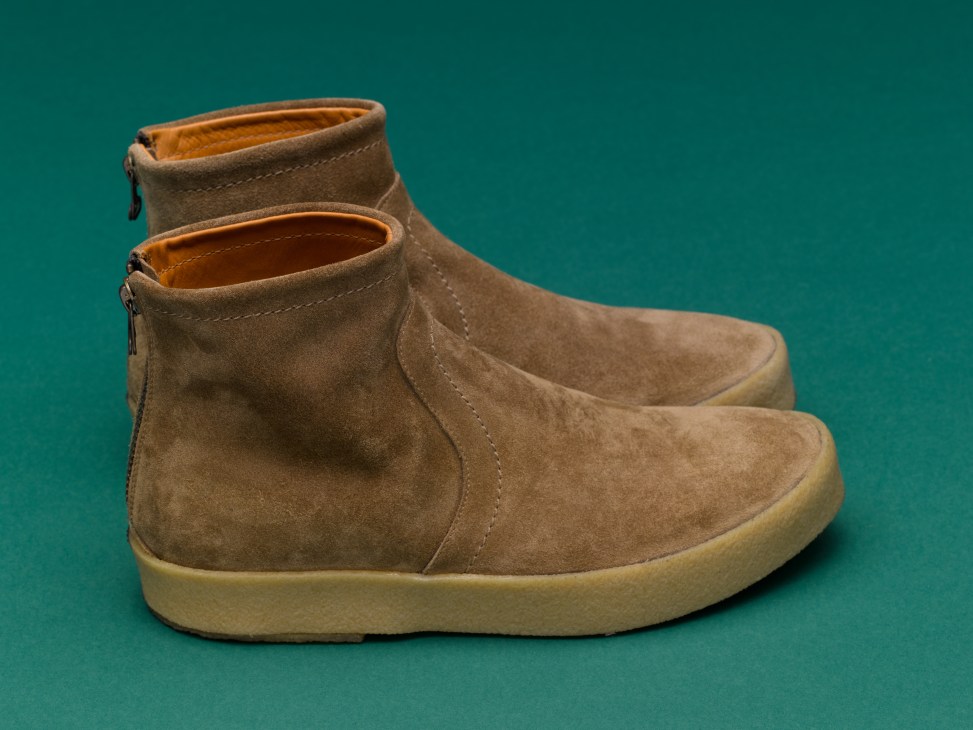Pair of tanned suede boots with cream-colored sole and orange inner lining against teal background.
