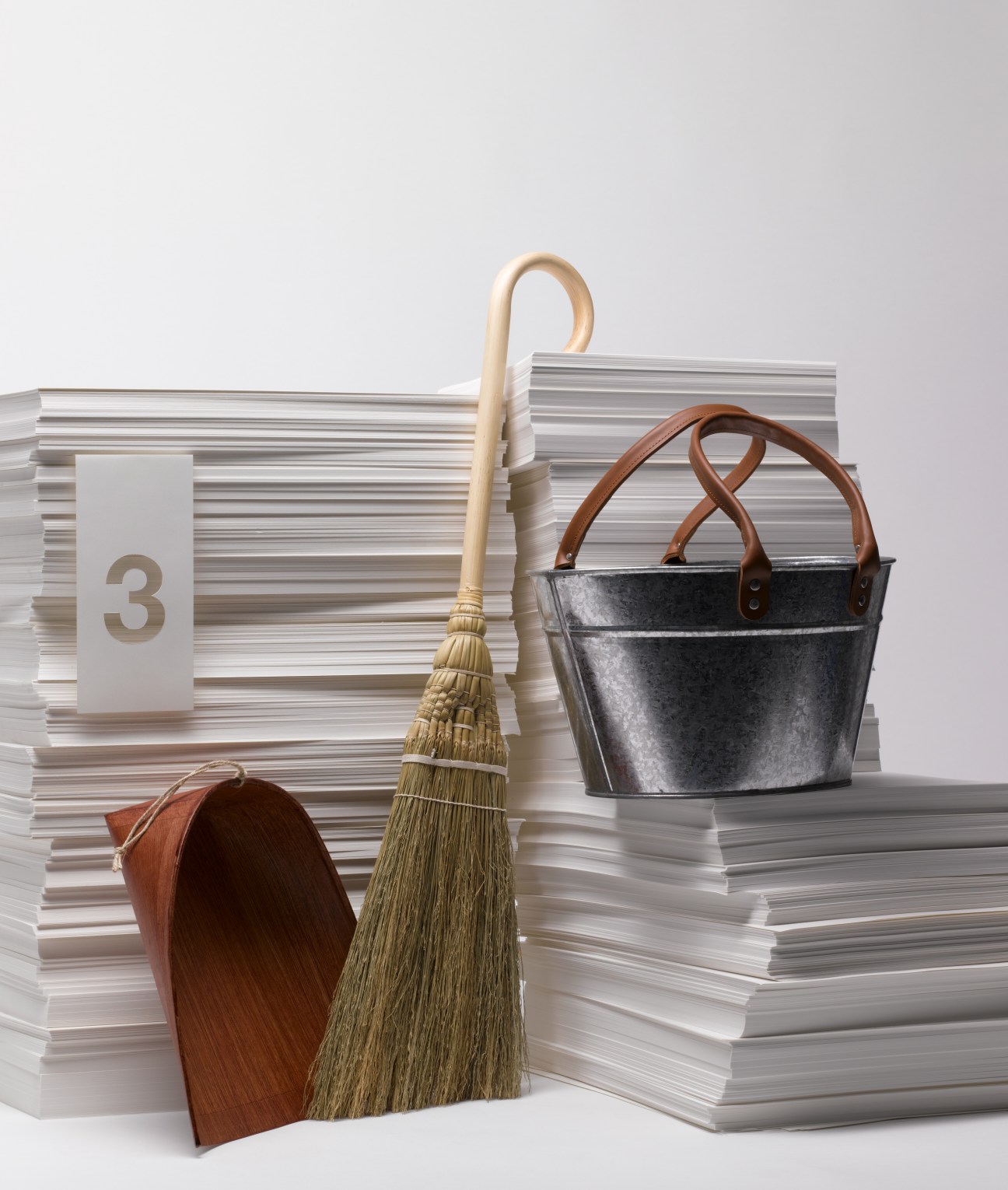 Sojirushi cleaning utensils arranged with stacked papers, including a rattan broom, dustpan, and metal baskets.