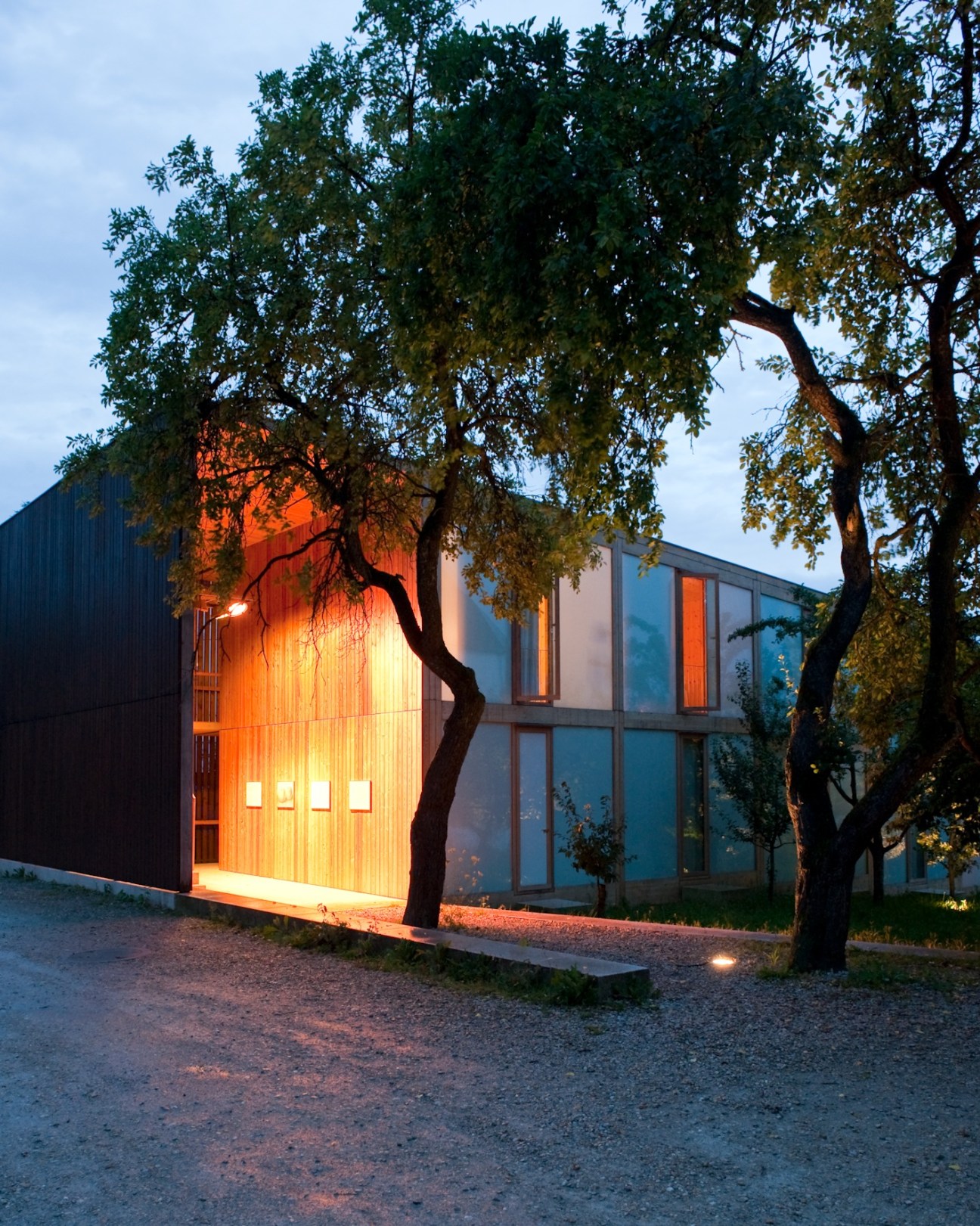 Modern eco-hotel building with wooden exterior lit from within at dusk, surrounded by mature trees.