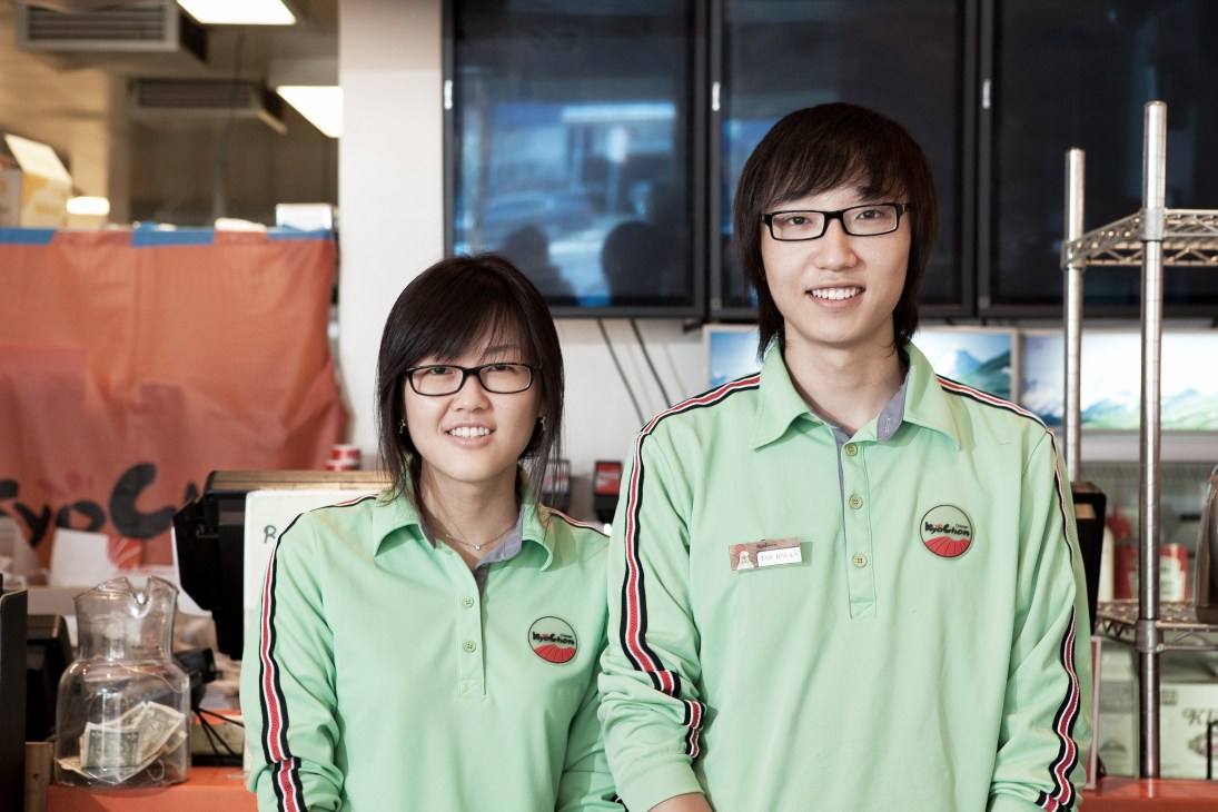 Two young staff members wearing matching green uniforms at Kyochon chicken restaurant in LA.