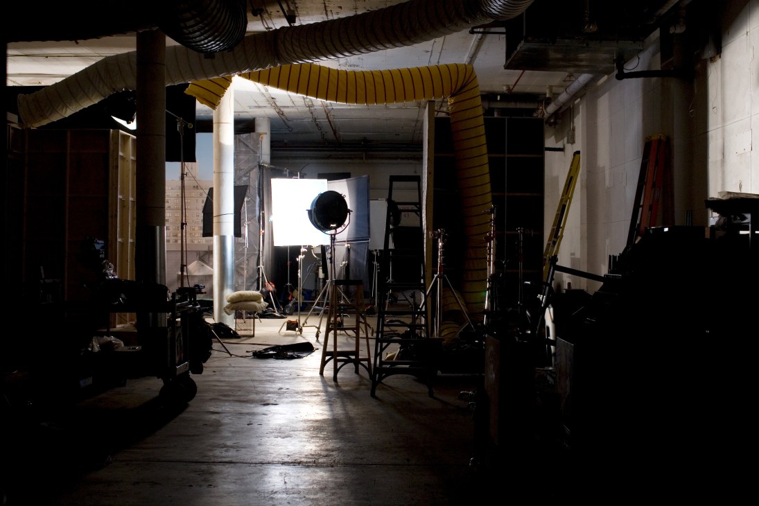 Film production set with professional lighting equipment and yellow ducts in an industrial warehouse space.
