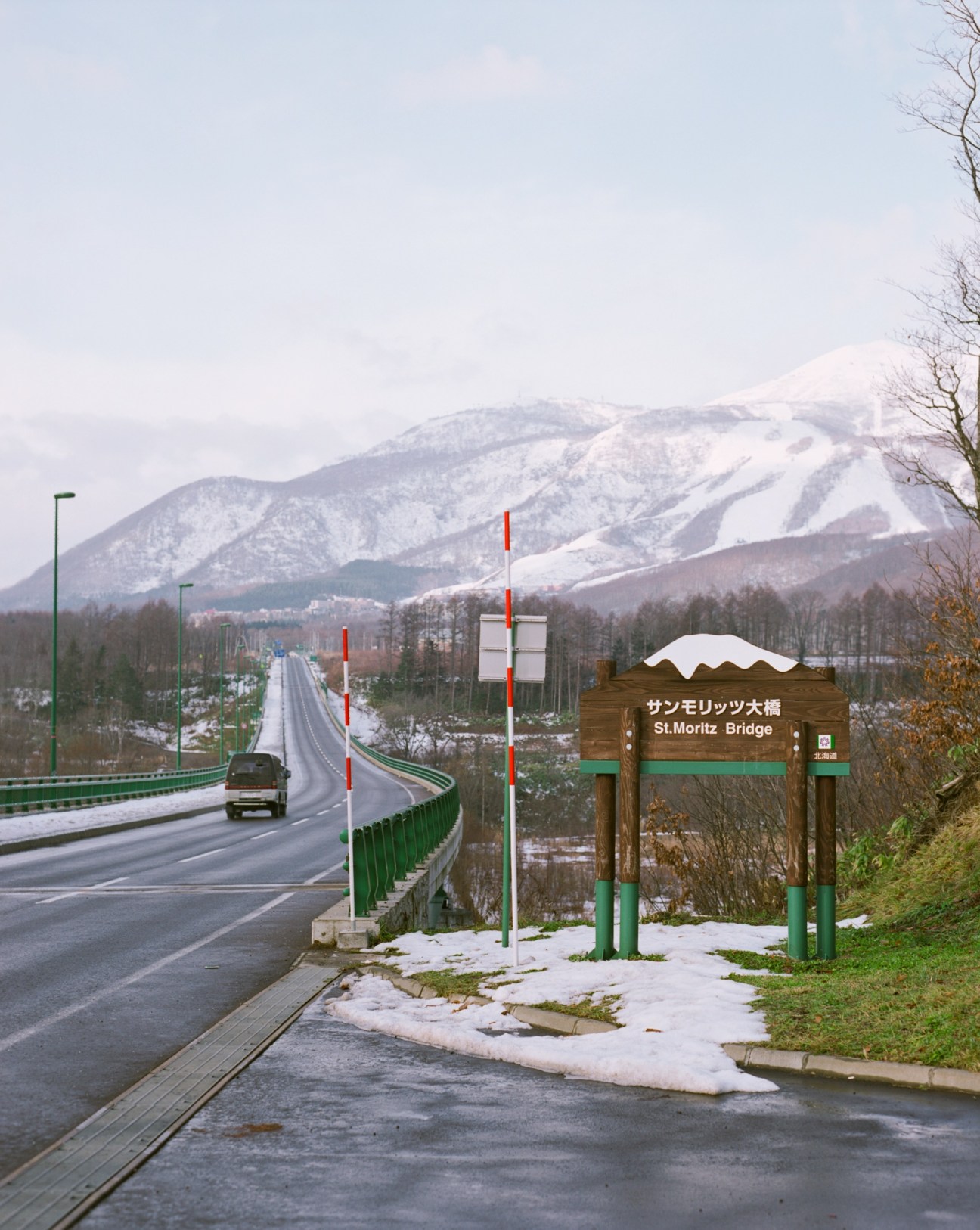 St Moritz Bridge spans a snow-covered valley with snow-capped mountains and forested slopes in the background.