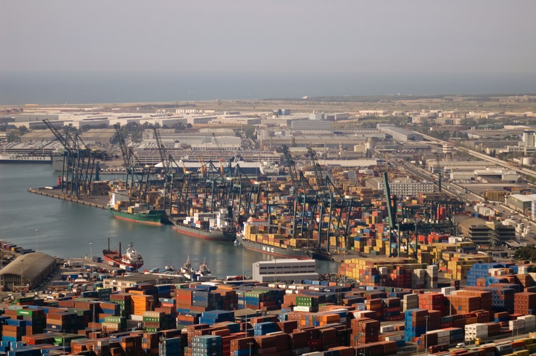 An MSC cargo ship laden with colorful stacked containers docked at Barcelona port with industrial cranes and warehouses.