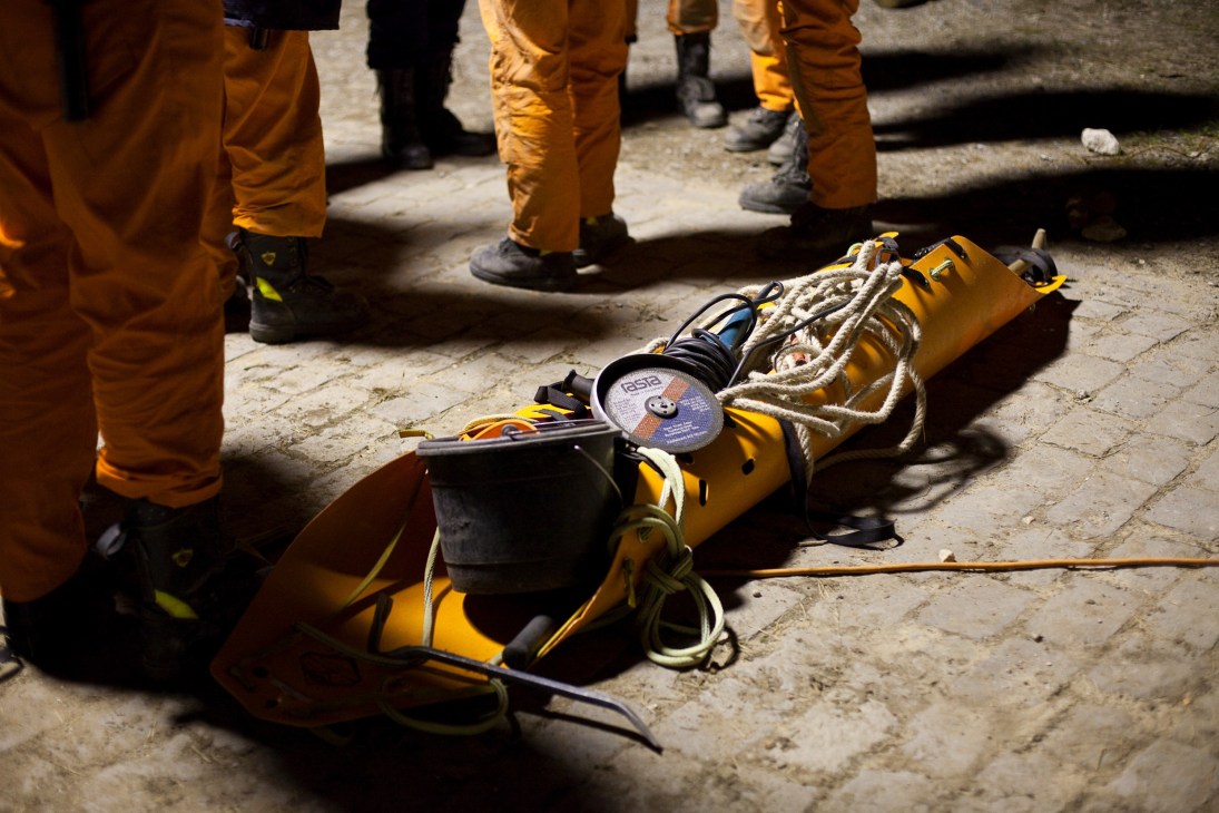 Yellow rescue equipment including cables and cutting tools laid on ground surrounded by workers in orange protective suits.
