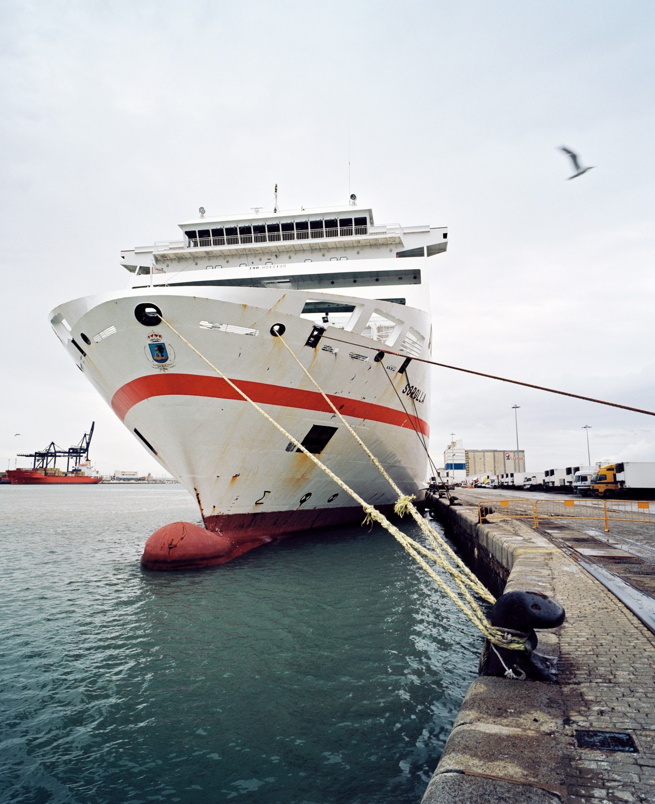 Large ferry ship docked at Cádiz harbour with red and white hull and mooring ropes.