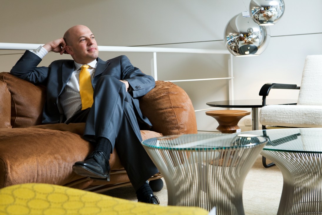 Daniel Schindler, CEO of Wohnbedarf, relaxes on a brown suede sofa in a modern showroom.