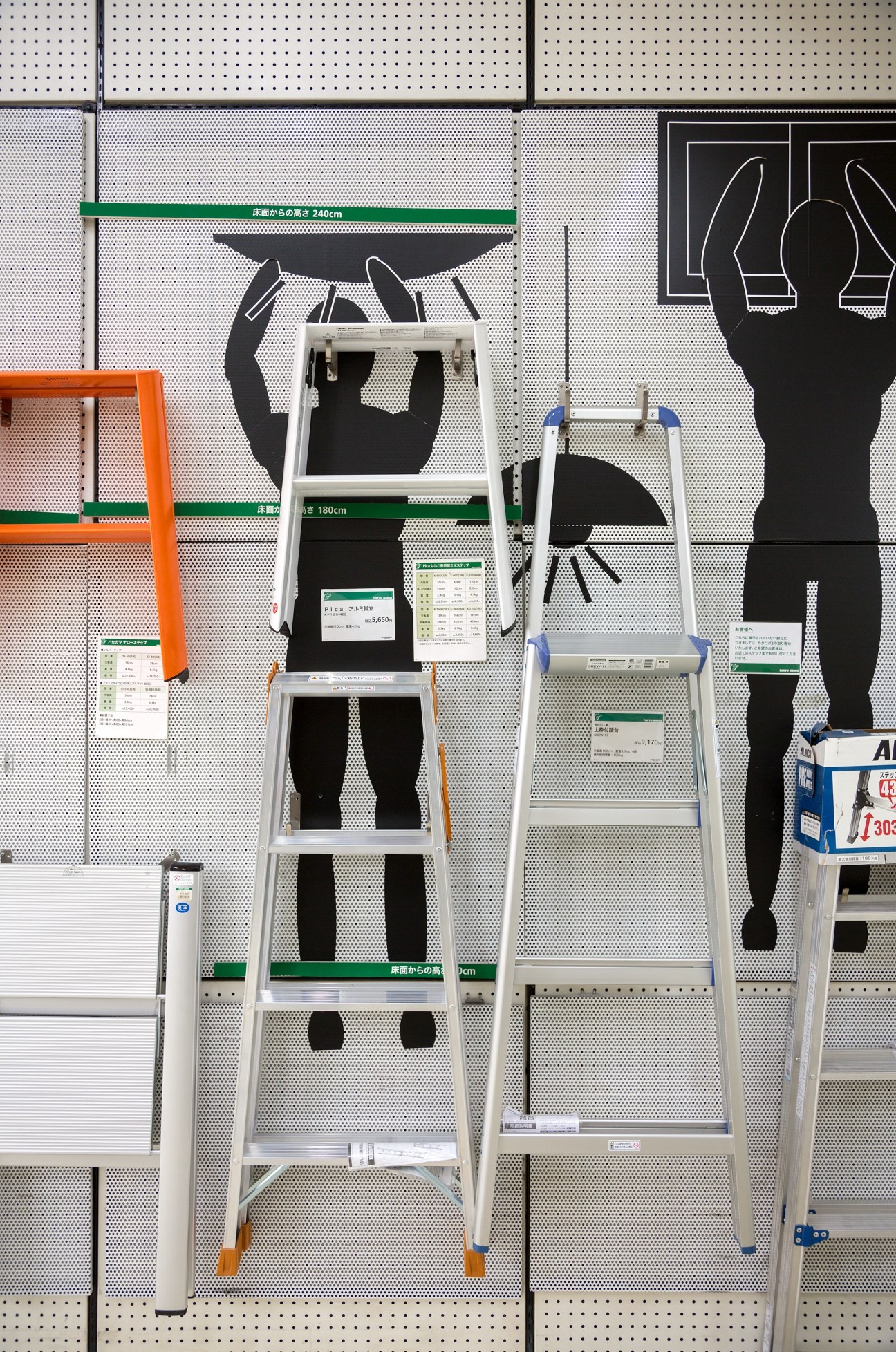 Aluminum ladders of various sizes displayed against pegboard wall with silhouette graphics and price labels.
