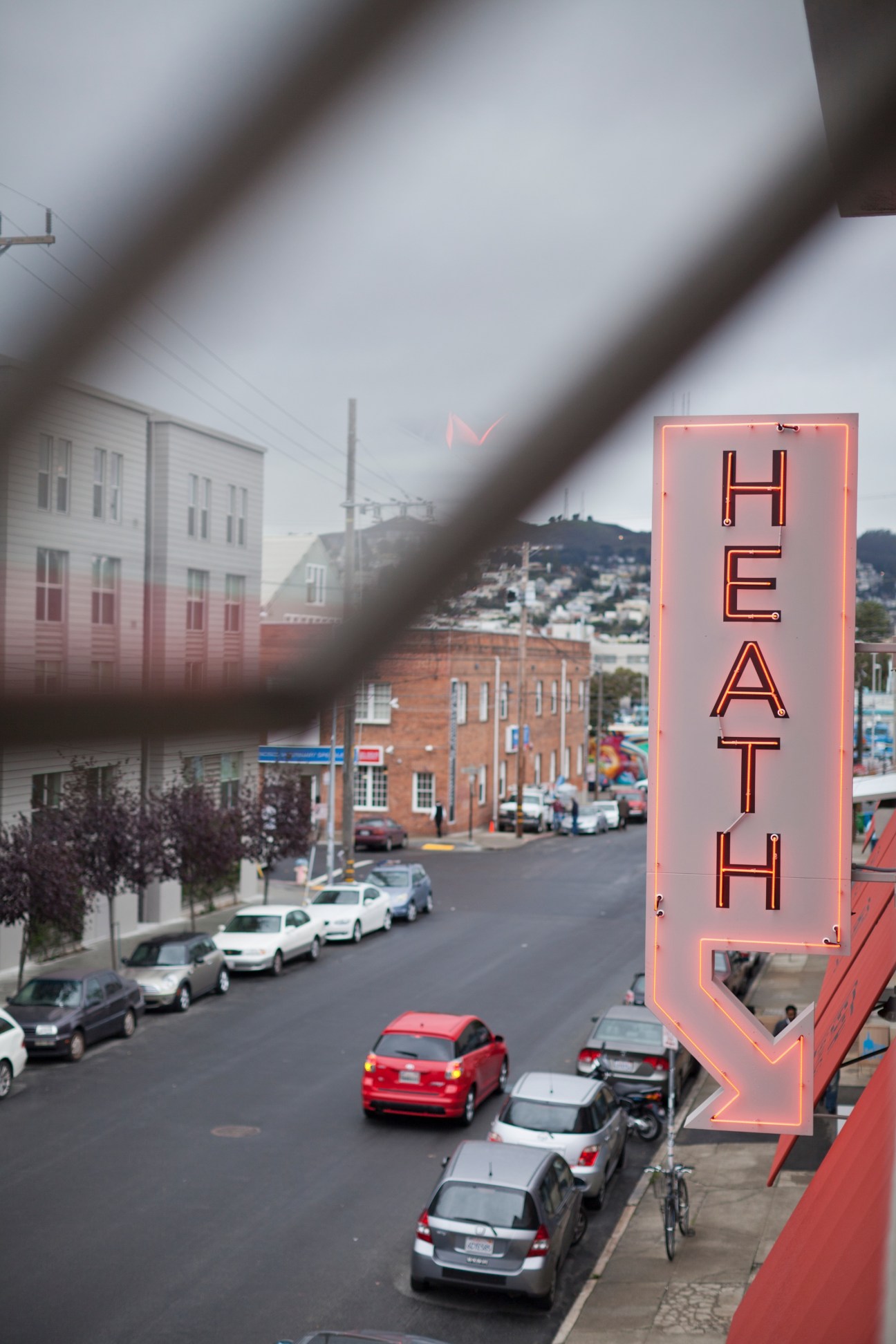 A neon HEATH sign glows pink-red above a San Francisco street with parked cars and brick buildings.
