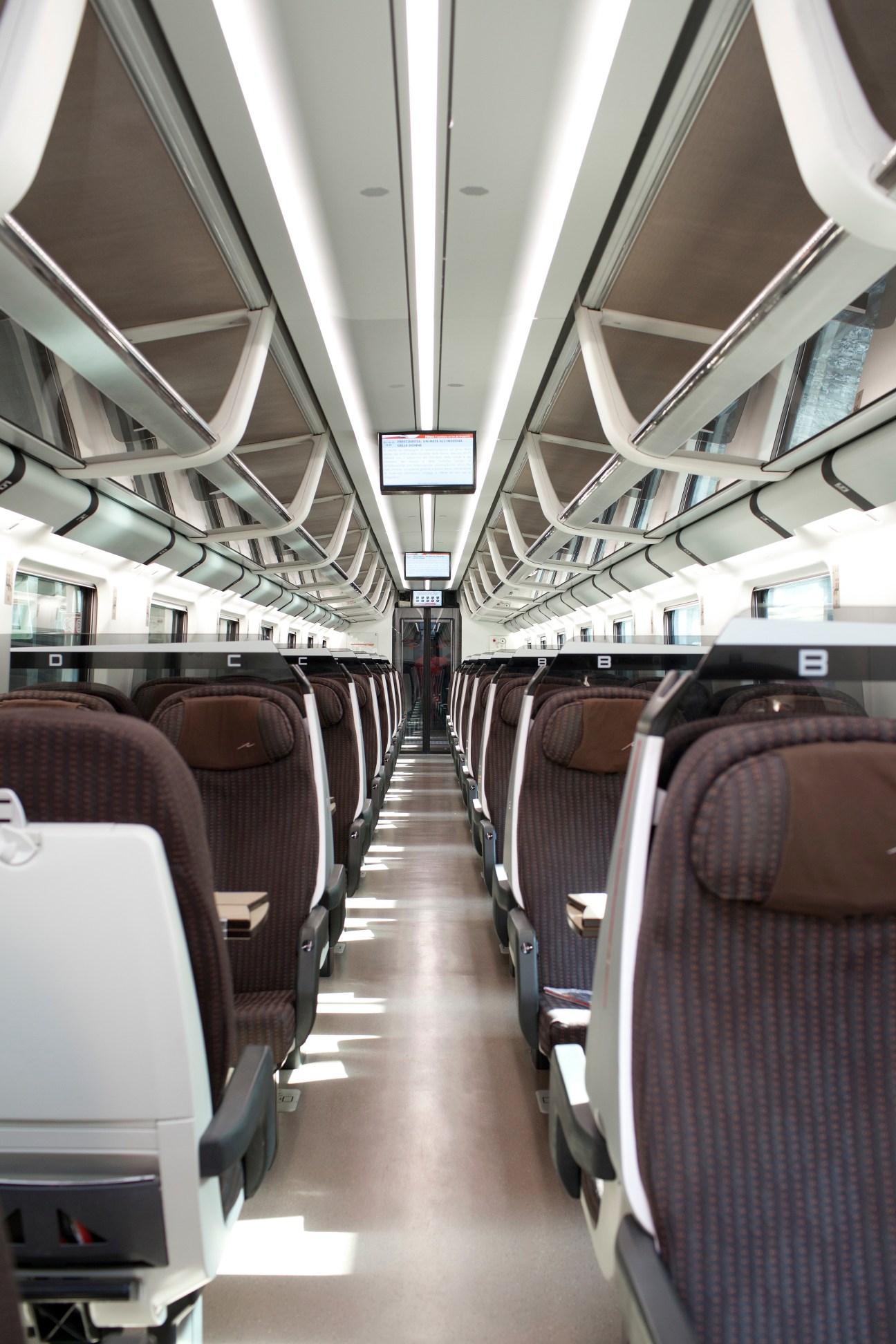 Interior of a modern train car with burgundy seats, white ceiling panels, and LED lighting running down the center.