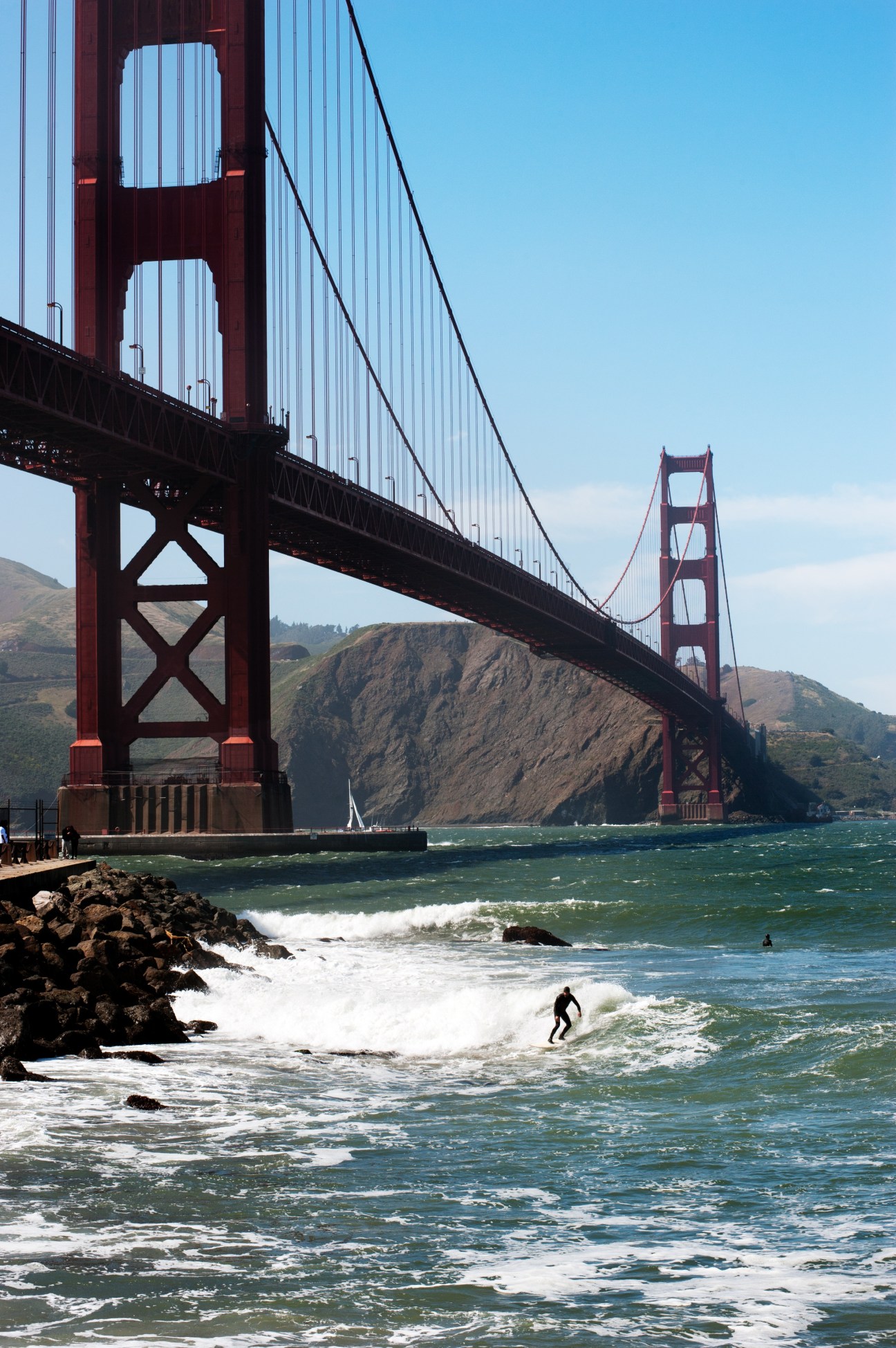 Surfer riding a wave at Fort Point with the Golden Gate Bridge towering in the background.