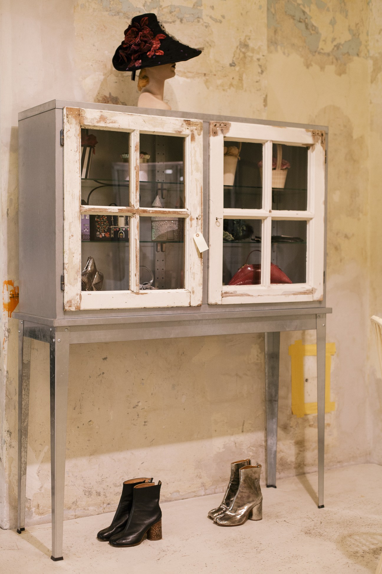 Display cabinet with glass doors showing fashion accessories and a mannequin wearing a black hat with red flowers.