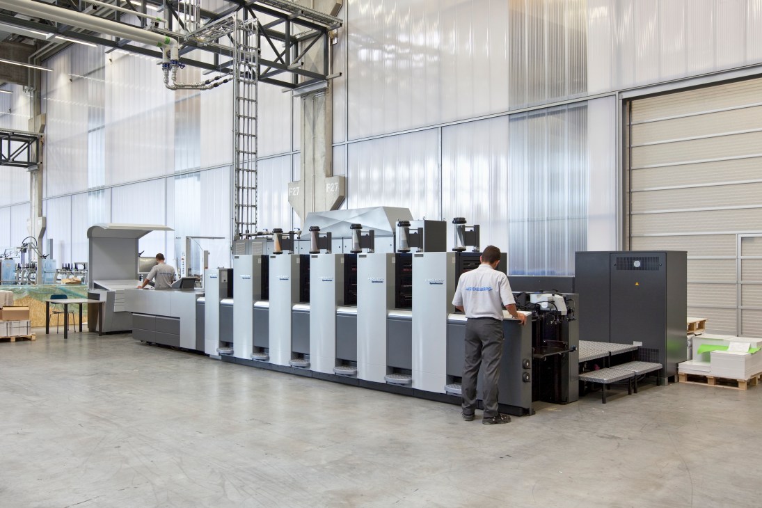 A Heidelberg Speedmaster printing press with technician operating controls in factory.