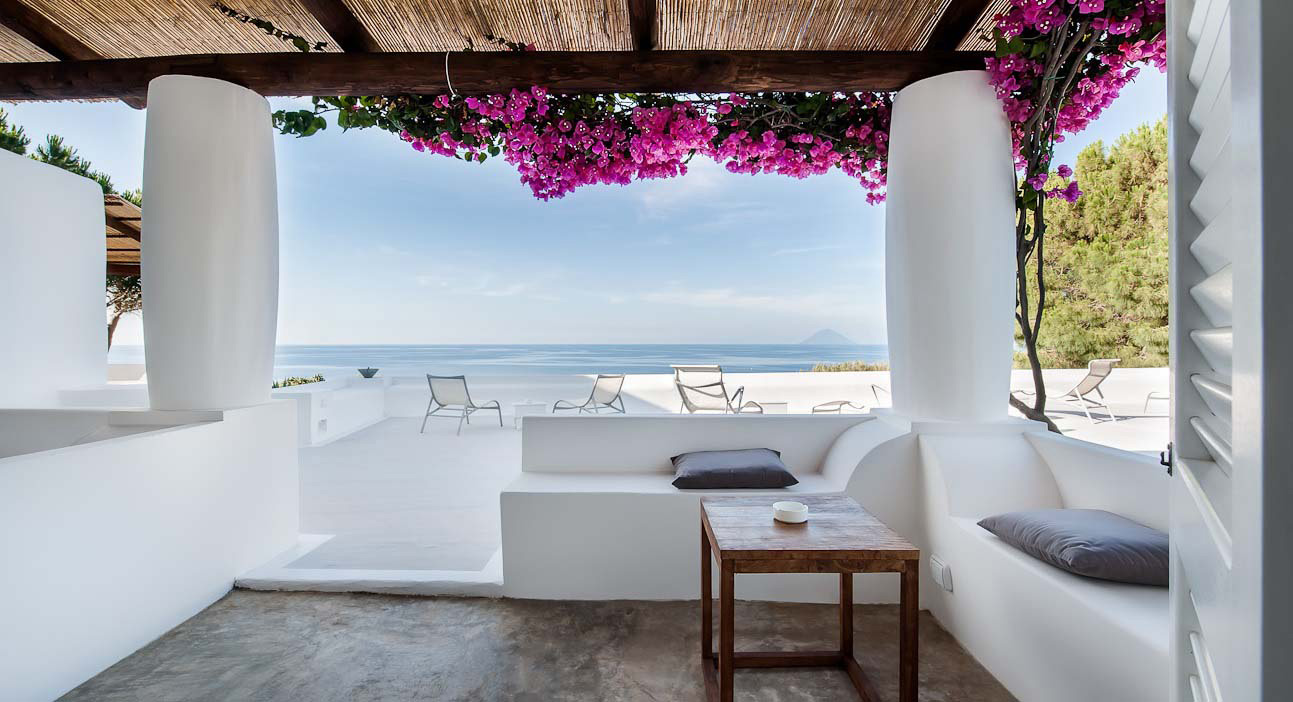 Whitewashed Mediterranean terrace with magenta bougainvillea, sea views, and lounge seating at Capofaro resort in Salina, Italy.