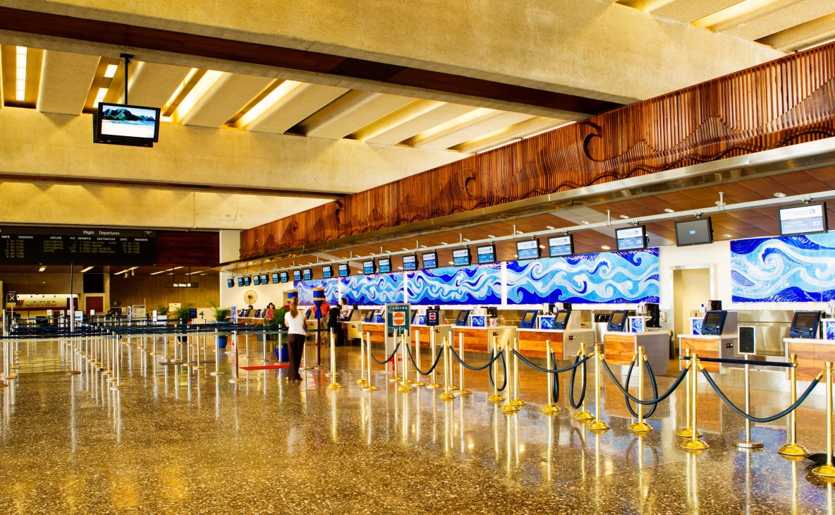 Honolulu airport check-in counter with warm wood paneling and blue wave mural decoration.