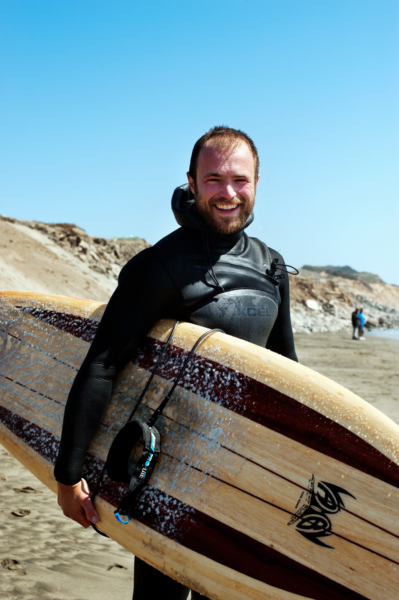 Surfer in wetsuit holding surfboard on San Francisco beach with cliffs in background