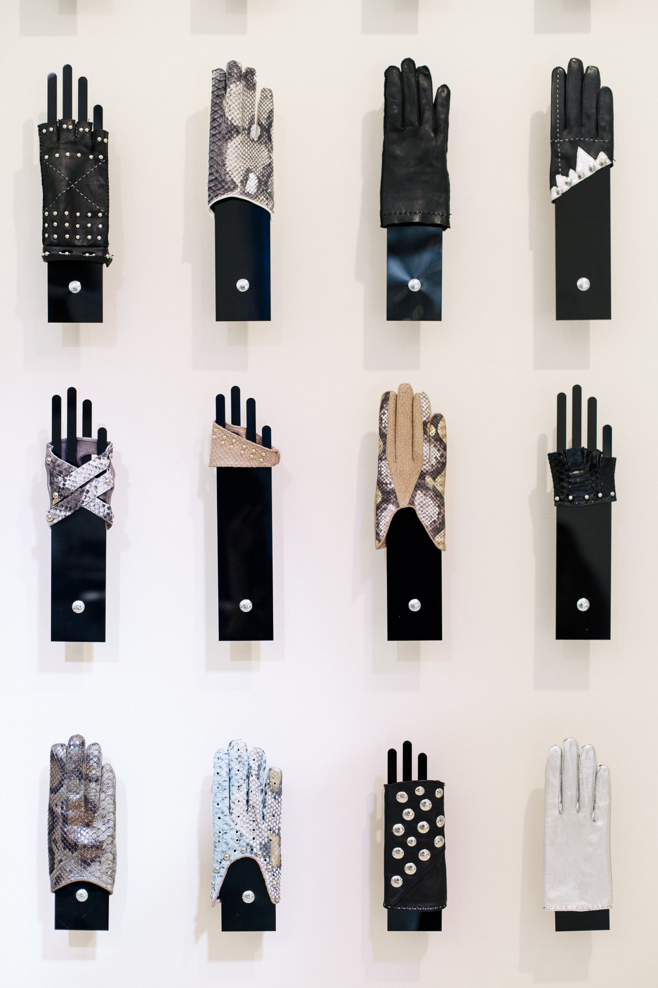 Display of twelve decorative gloves in various styles and colors mounted on white wall.