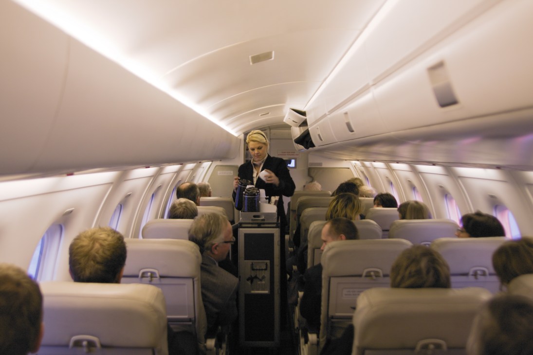 A flight attendant serves passengers inside a Krohn Air turboprop aircraft cabin.